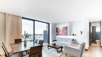 Una sala de estar moderna con comedor, ventanas amplias, un sofá gris y vistas a la ciudad.