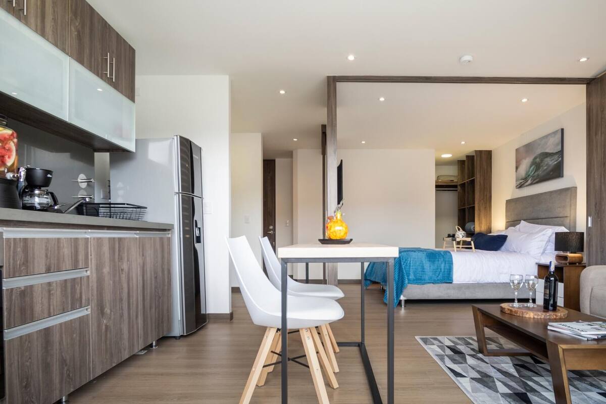 Quarto de hotel moderno com cozinha compacta, espaço para refeições, cama e área de estar.