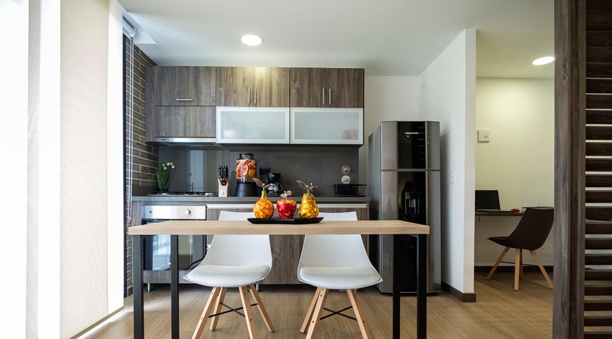 Une cuisine moderne avec un coin repas, comprenant une table en bois, deux chaises blanches et un réfrigérateur.