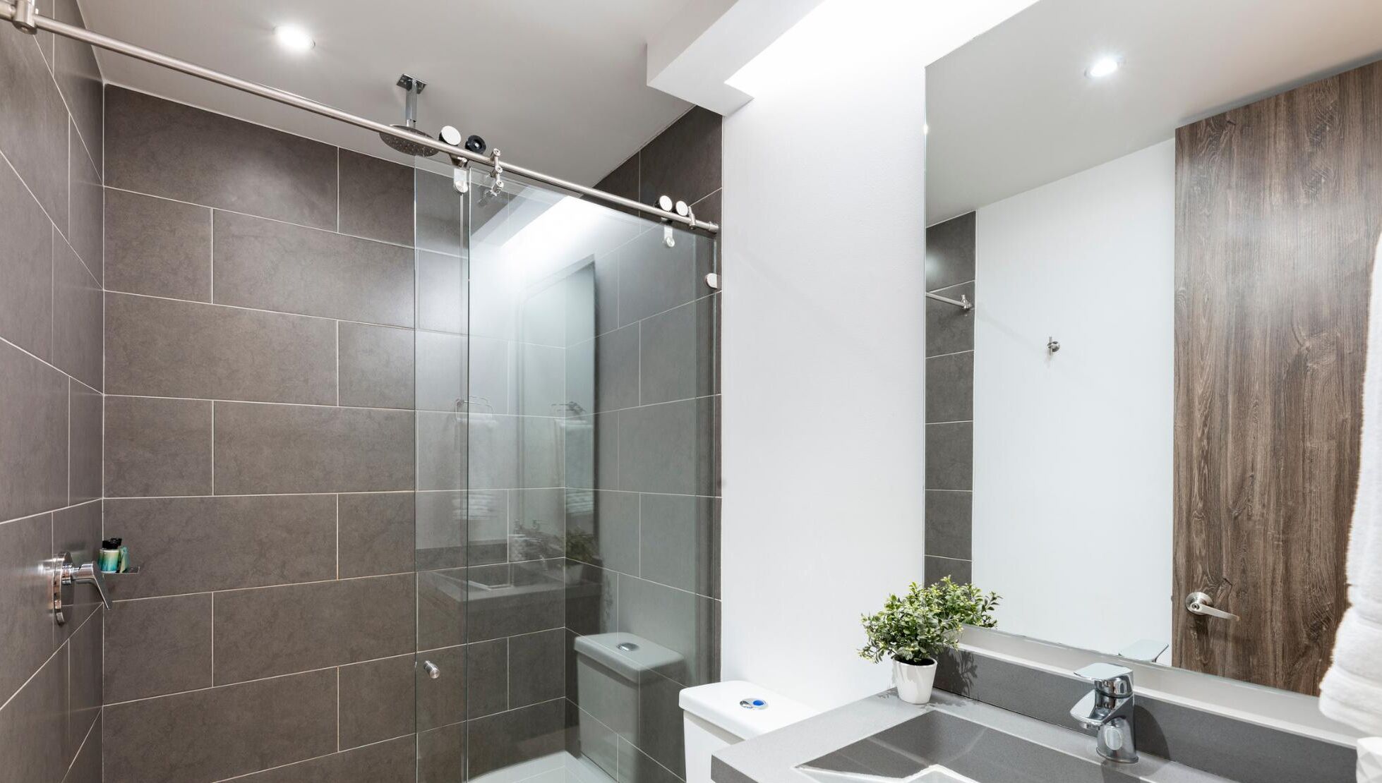 A modern bathroom with a glass shower enclosure, a wooden vanity, and a large mirror.