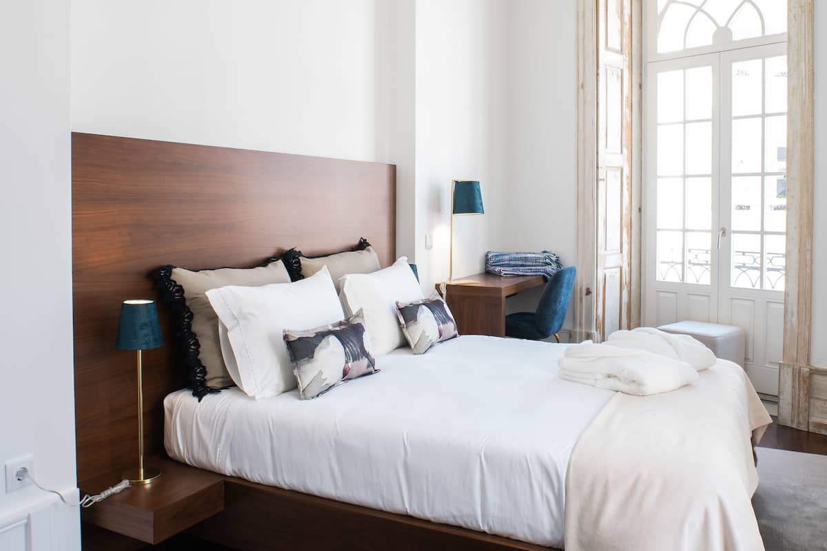 A modern bedroom with a wooden headboard, a desk, and a large window.