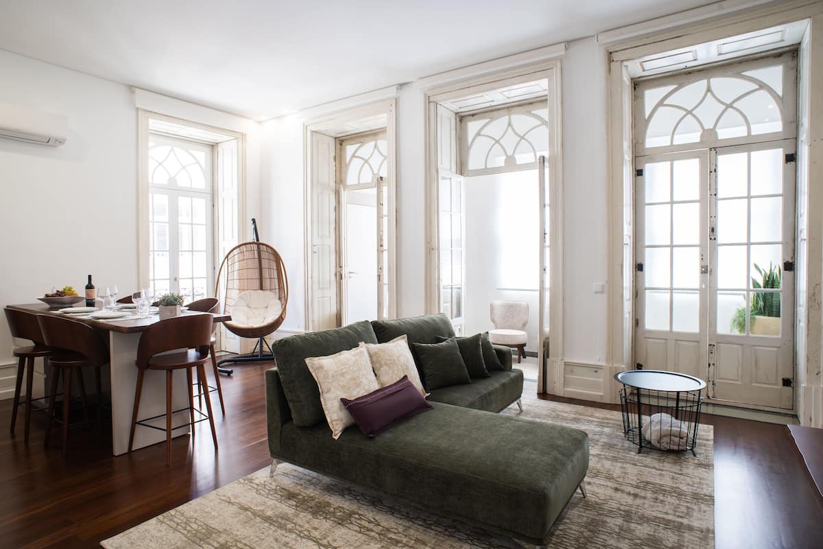 A spacious living room with a green sofa, a dining area with wooden chairs, and large windows with decorative glass panels.