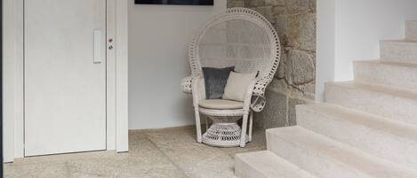 Un interior moderno con una pared de piedra, una puerta blanca, un sillón de mimbre blanco y una escalera.