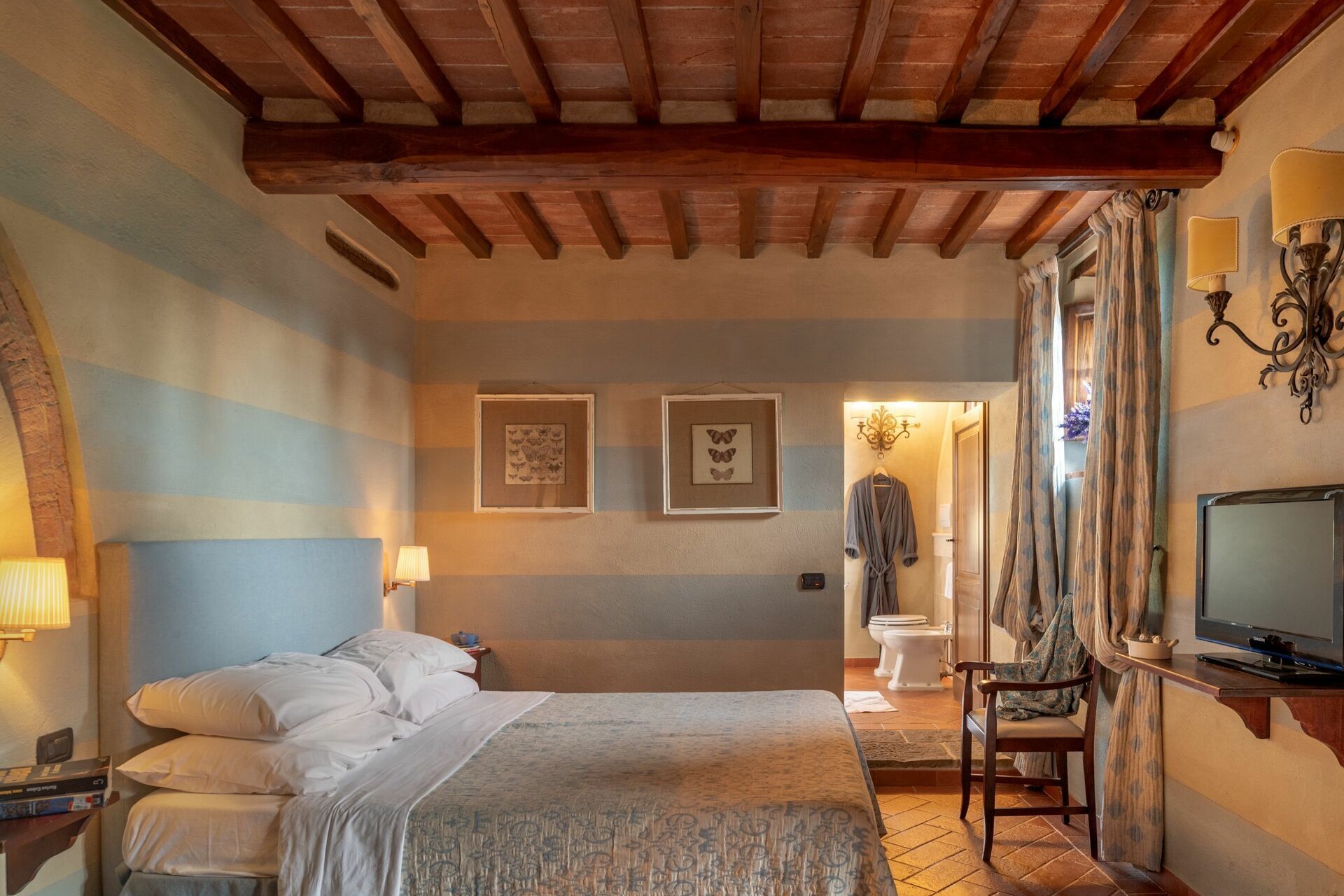 A hotel room with a bed, bedside lamps, a television, and a bathroom visible through an open door.