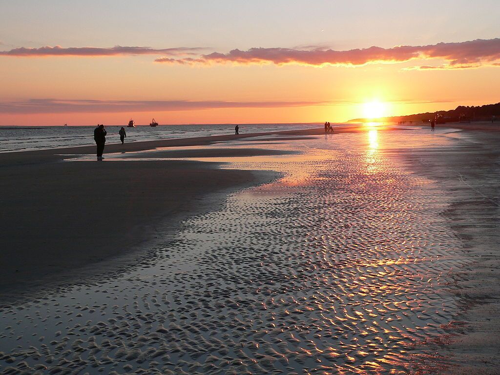 A beach at sunset with people walking along the shore.