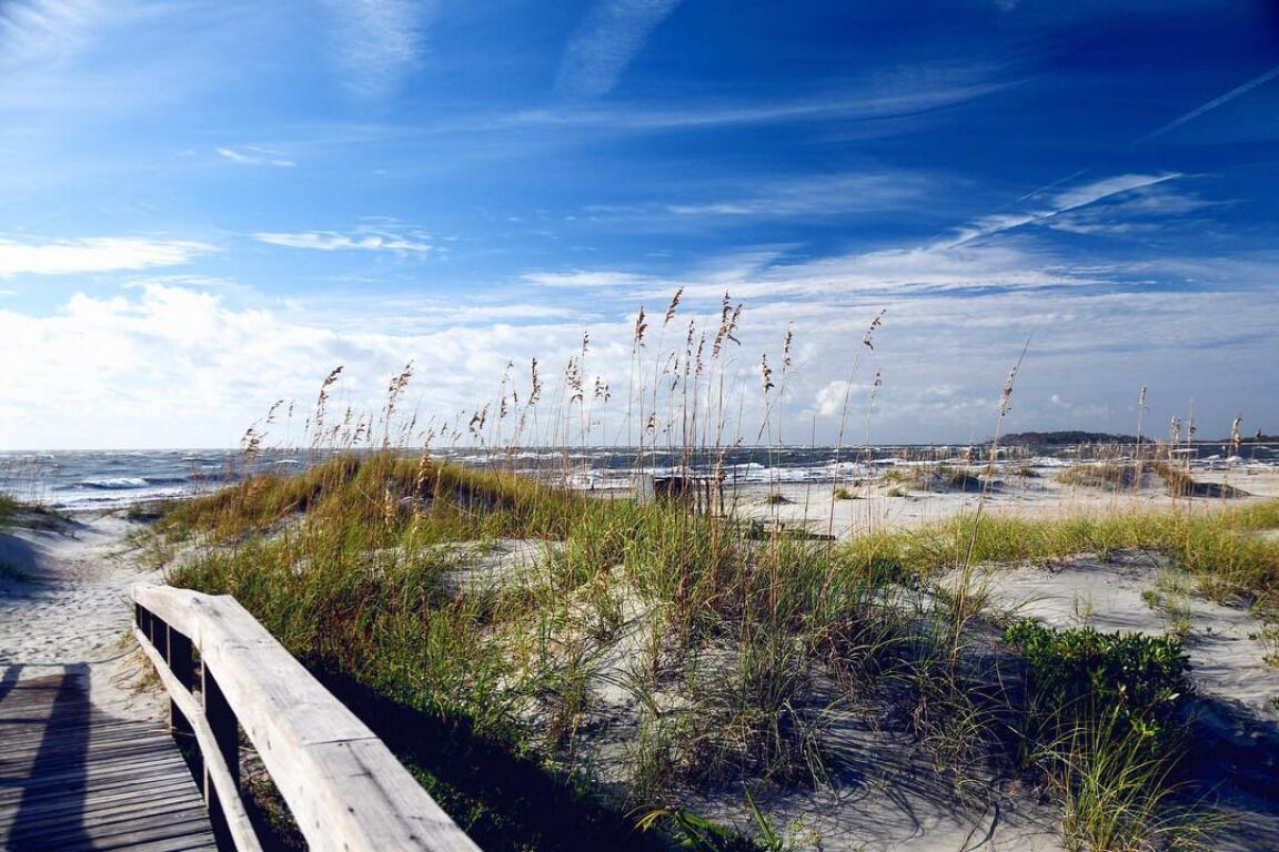 A wooden boardwalk leading to a beach with sand dunes and sparse vegetation.