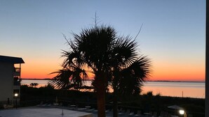 A pool area with lounge chairs and umbrellas, a palm tree, and a view of the sunset over the water. - Tybee Island Ocean Therapy (Tybee Island)