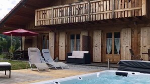 A wooden cabin with a hot tub and lounge chairs by the pool.