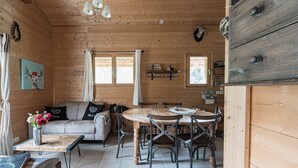A cozy cabin interior with a wooden dining table, a sofa, and a chandelier.