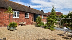 A brick house with a gravel driveway and a garden with potted plants and a wooden fence. - Daisy (Rye)