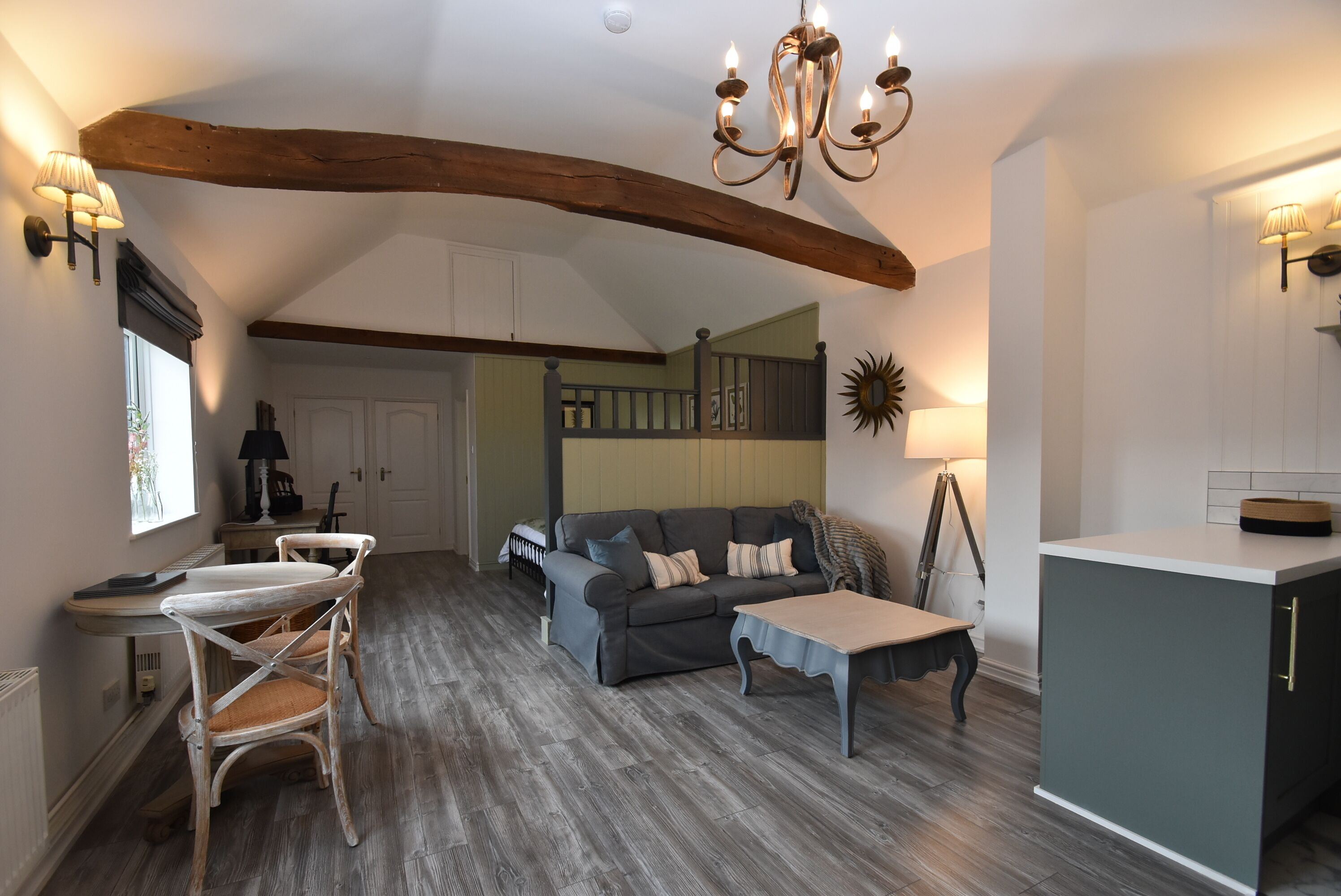 A spacious living area with a high ceiling, a dining table with chairs, a sofa, and a kitchen area with cabinets and a countertop.