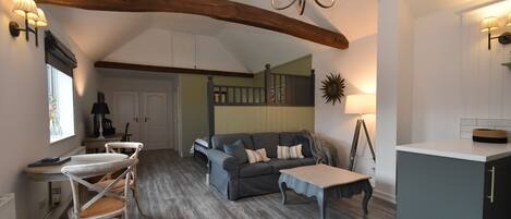 A spacious living area with a high ceiling, a dining table with chairs, a sofa, and a kitchen area with cabinets and a countertop.