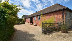 A red brick house with a gravel driveway and a wooden gate. - Daisy (Rye)