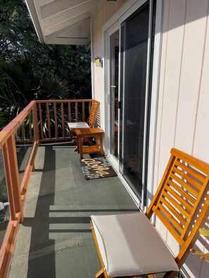 A balcony with wooden railings, a sliding glass door, and two lounge chairs with cushions.