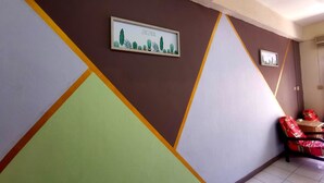 Um corredor com desenhos geométricos nas paredes e um quadro com cactos. Há duas cadeiras com almofadas vermelhas.