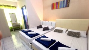 Quarto de hotel com três camas de solteiro, cada uma com um cobertor azul e uma toalha branca. Há uma pintura abstrata colorida na parede acima das camas.