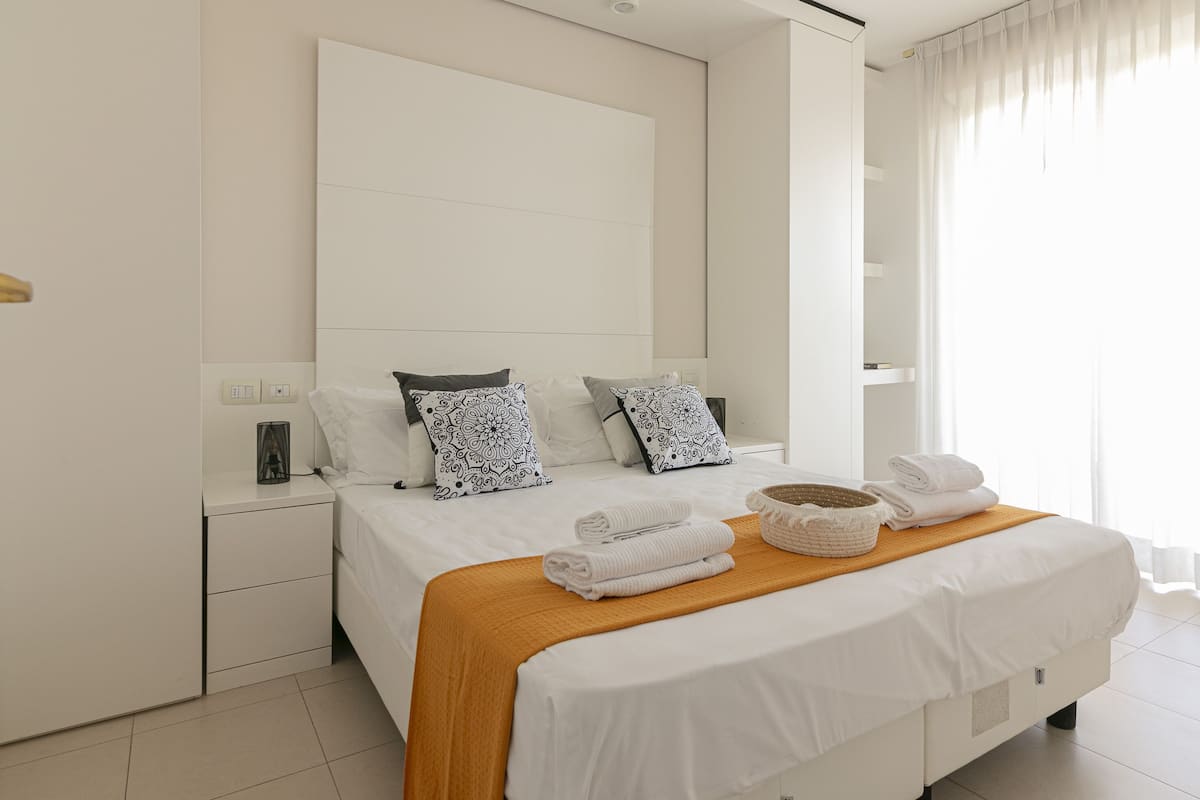 A modern hotel room with a large bed, a wooden headboard, and a bedside table with a lamp.