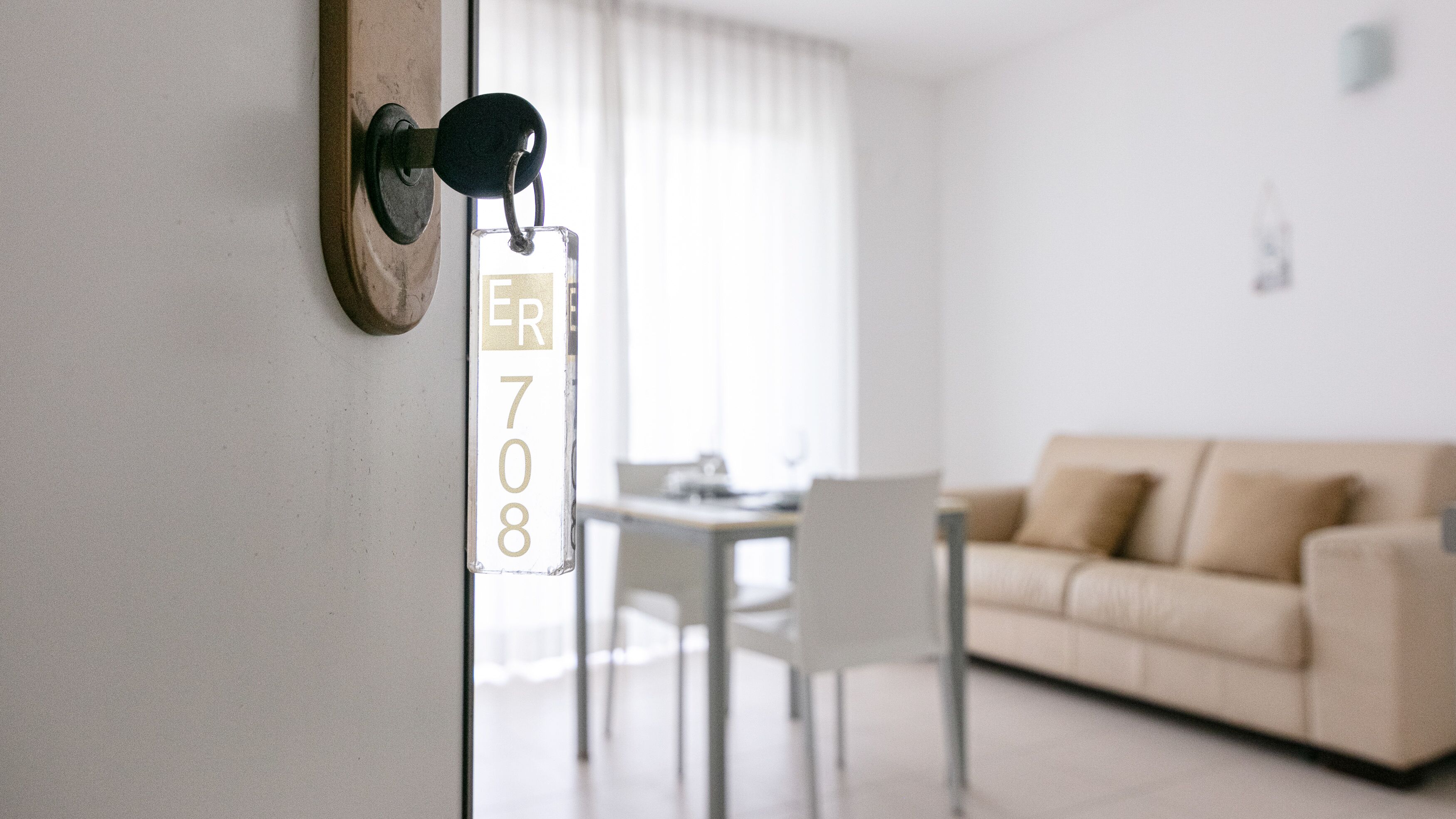 A modern interior with a beige sofa, a dining table, and a door with a keycard reader labeled "ER 708".