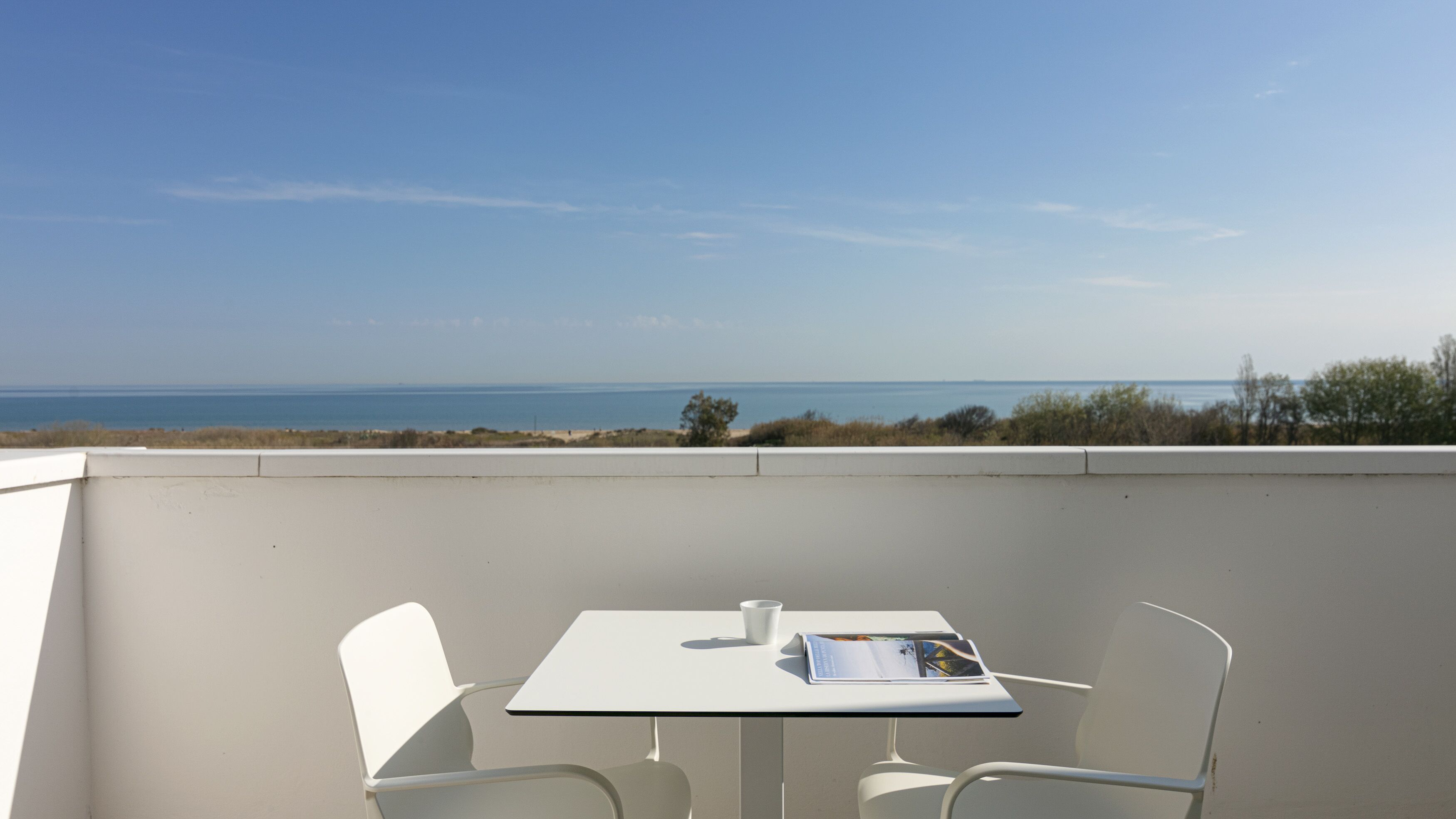 A balcony with a table and chairs, overlooking a beach and ocean.
