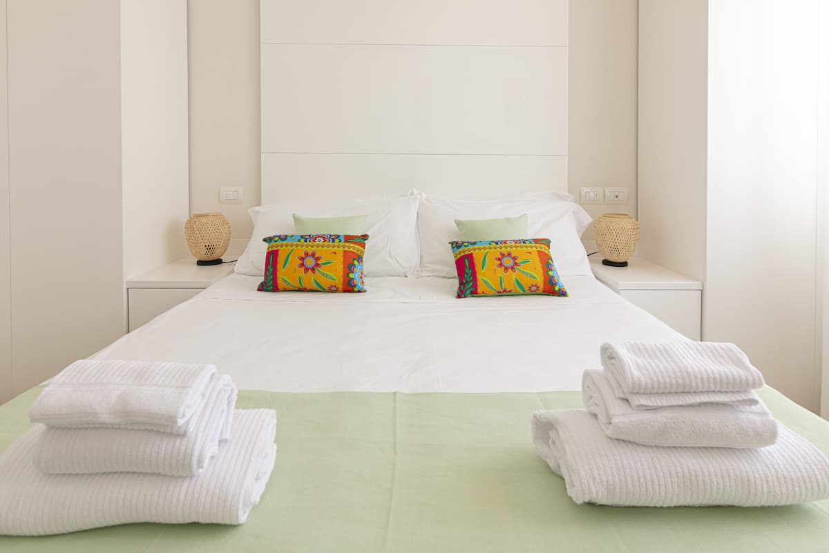 A hotel room with a large bed, two pillows, two bedside tables, and two lamps.