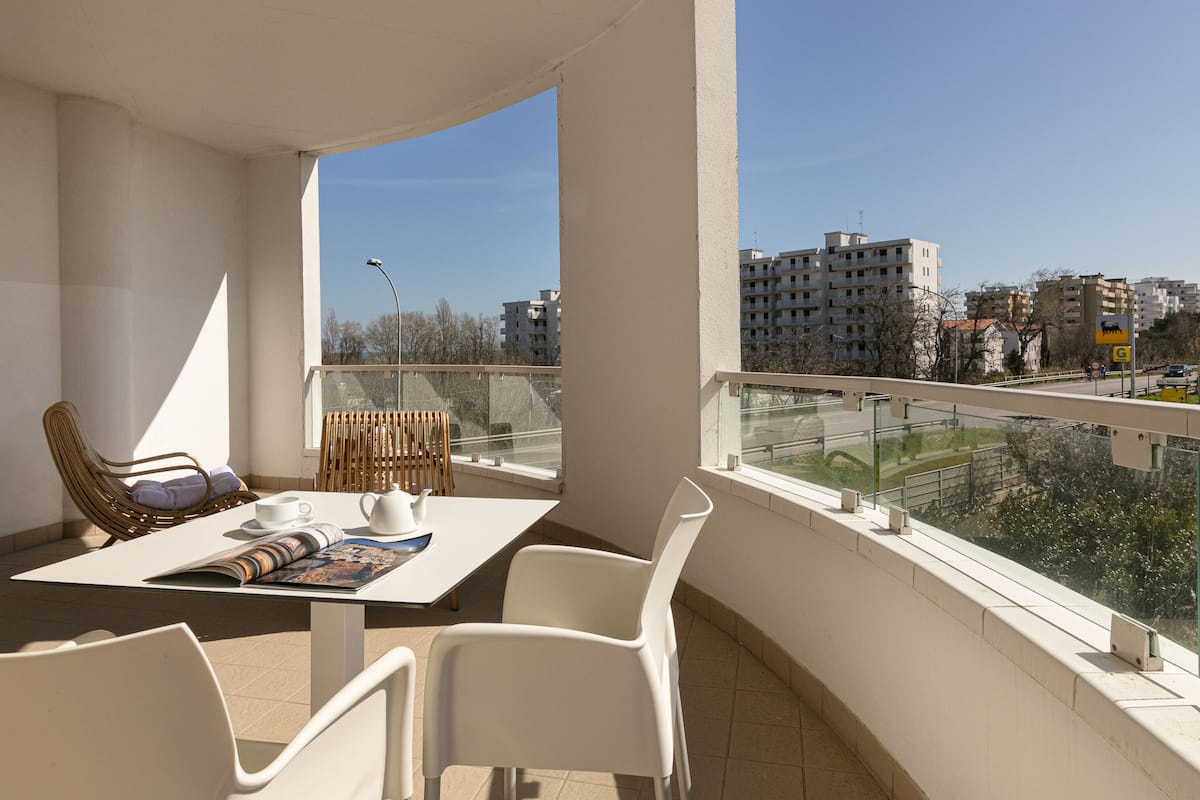 A balcony with a table, chairs, a wicker chair, and a view of buildings.
