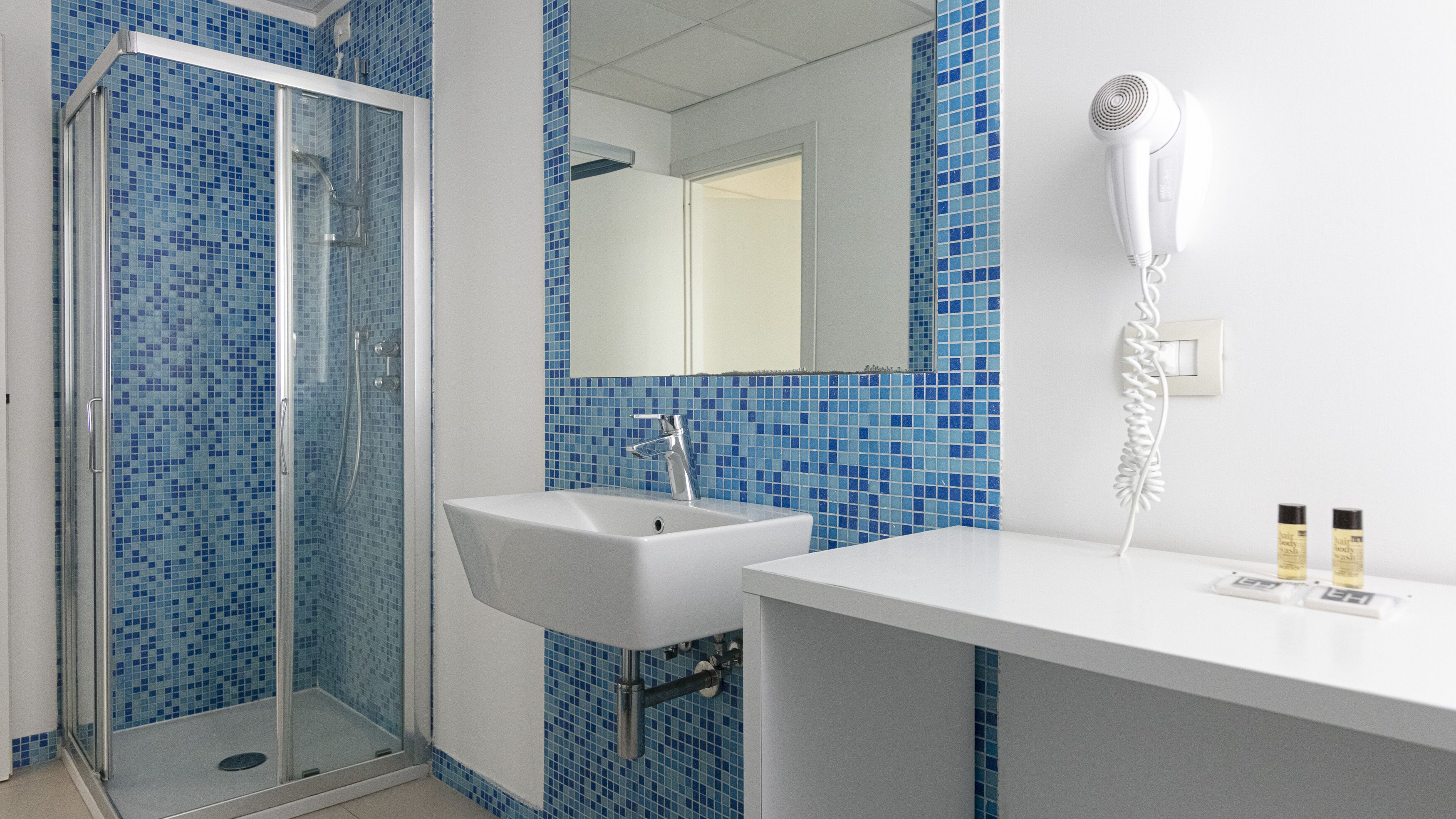 A bathroom with a glass shower enclosure, a sink, and a hairdryer mounted on the wall.