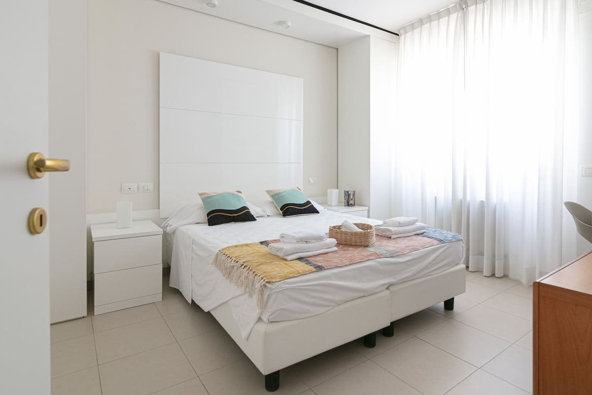 A modern bedroom with a large bed, bedside tables, a desk, and a wardrobe.
