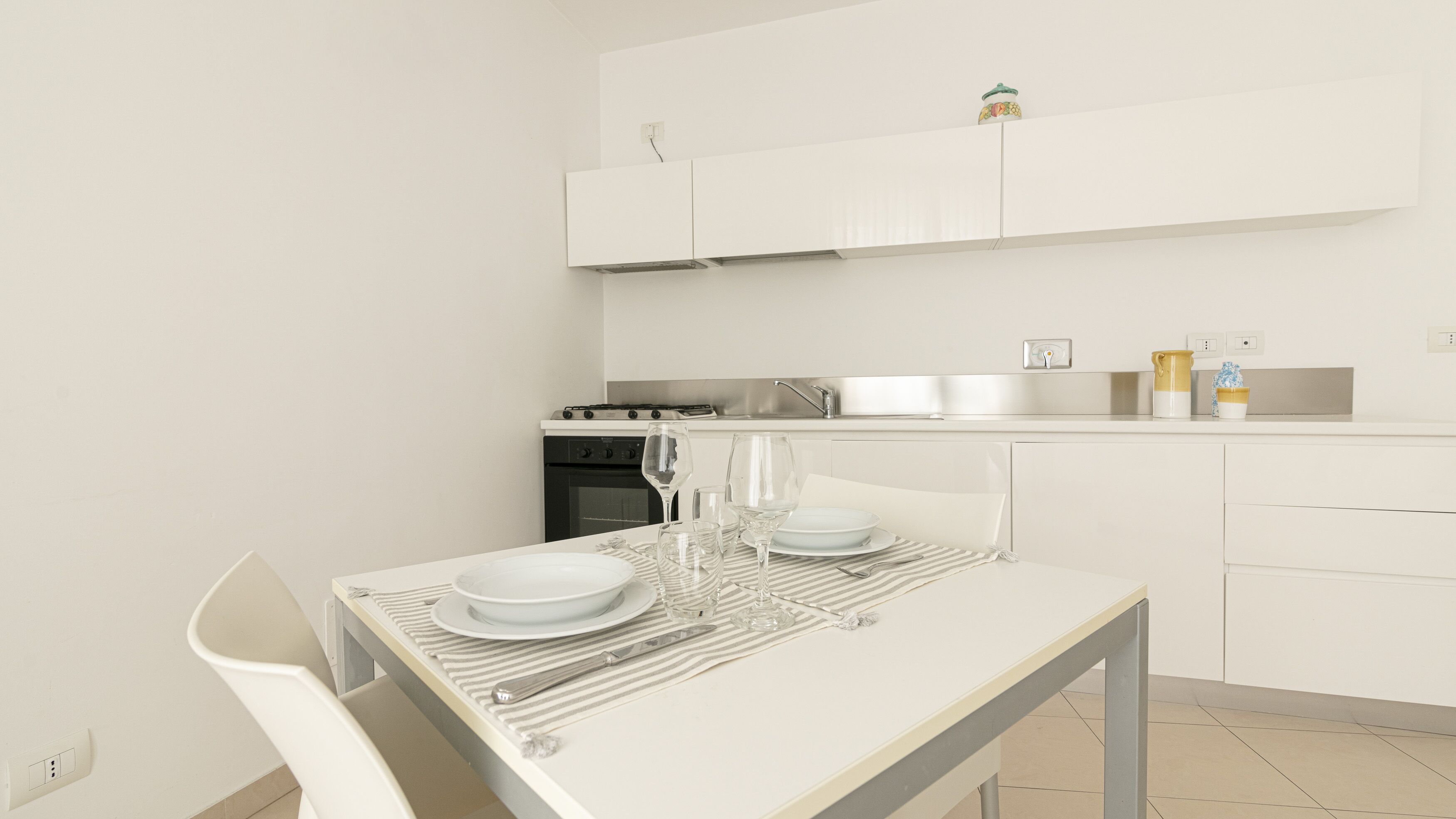 A modern kitchen with white cabinetry, a stainless steel range, and a dining area with a white table set for two.