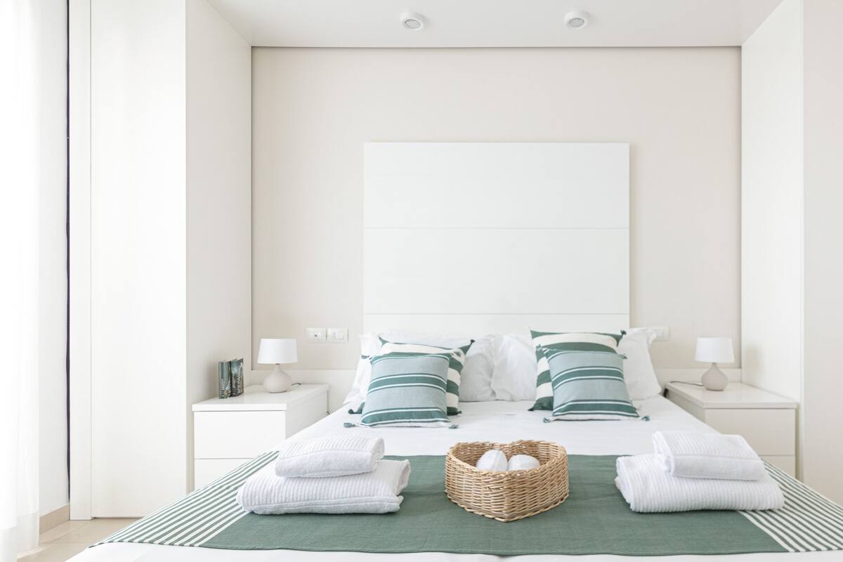 A minimalist hotel room with a large bed, two bedside tables, and a green-striped area rug.