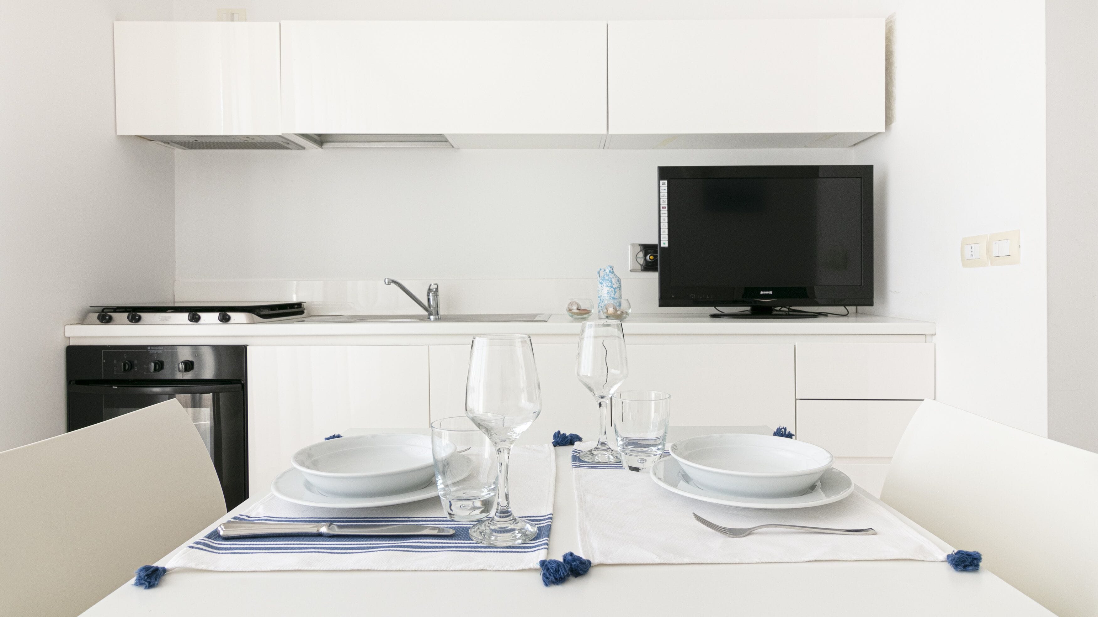Une cuisine moderne avec des meubles blancs, une cuisinière et un téléviseur à écran plat.