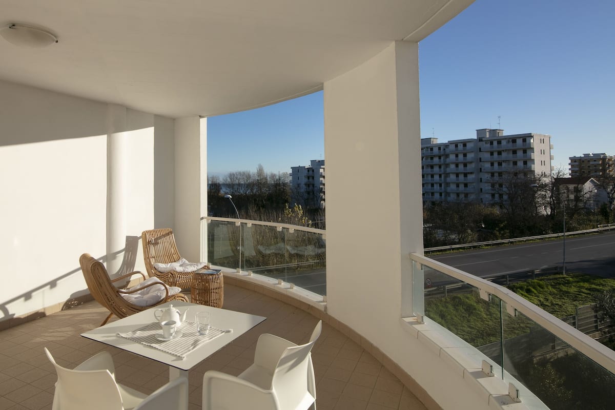 A balcony with a table and chairs, a view of a road and buildings in the distance.