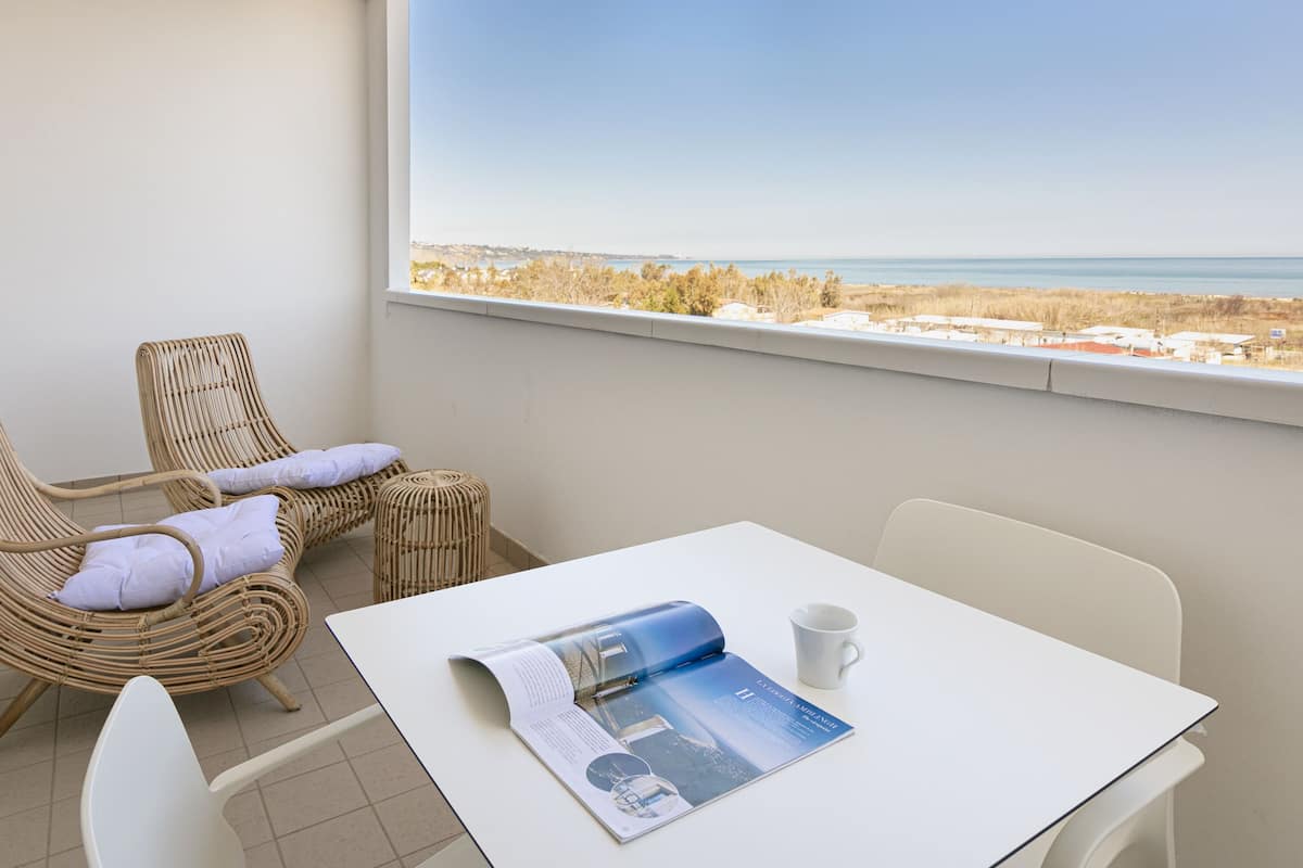 A balcony with wicker chairs, a table, and a view of the sea.