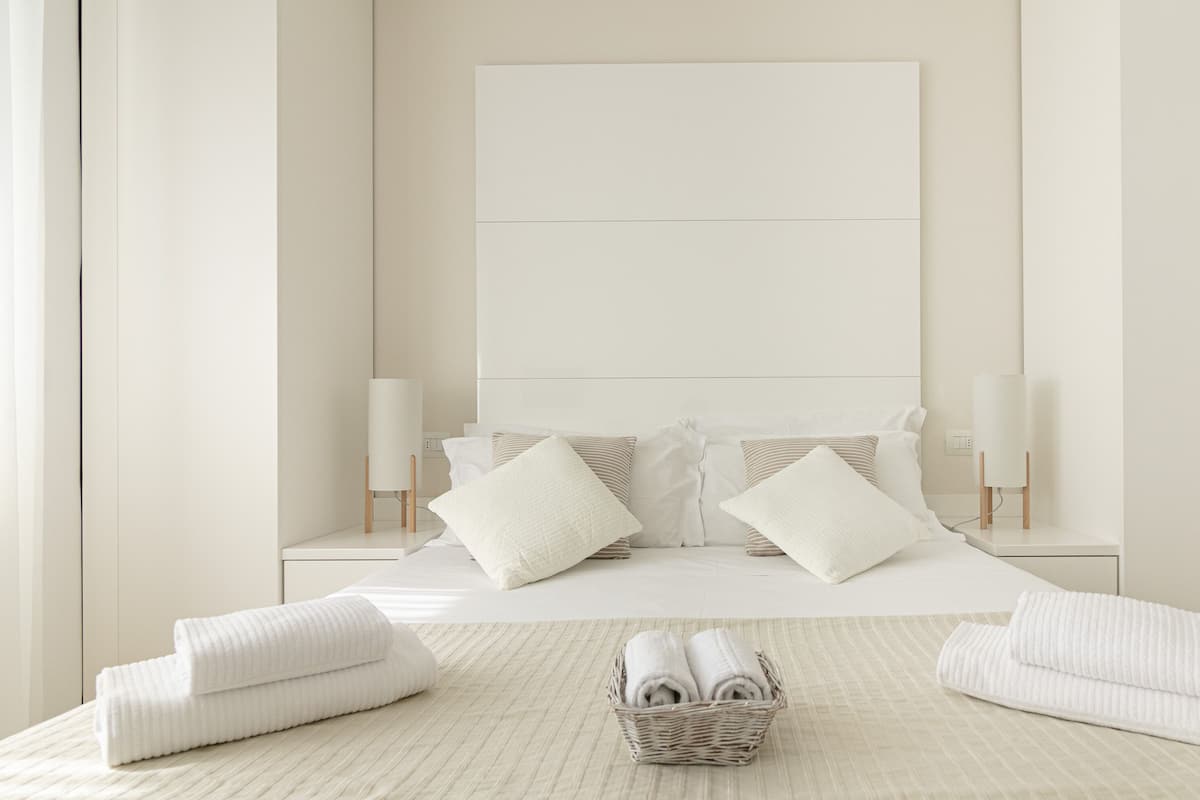 A minimalist bedroom with a large bed, two bedside lamps, and a bedside table with a lamp.