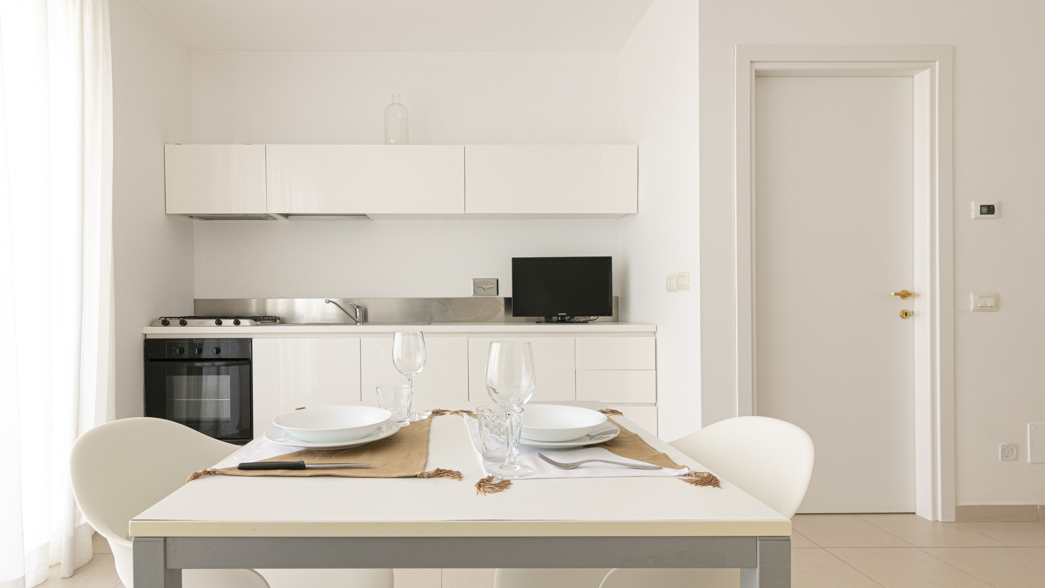 A modern kitchen with white cabinetry, a built-in oven, and a television.