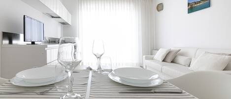 Un salon moderne et bien éclairé, avec un coin repas aménagé pour deux personnes, comprenant une nappe à rayures, des assiettes blanches et de la verrerie transparente.