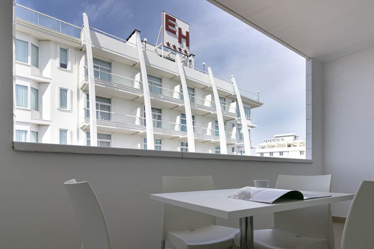 A hotel room with a balcony, a white table, and four white chairs.