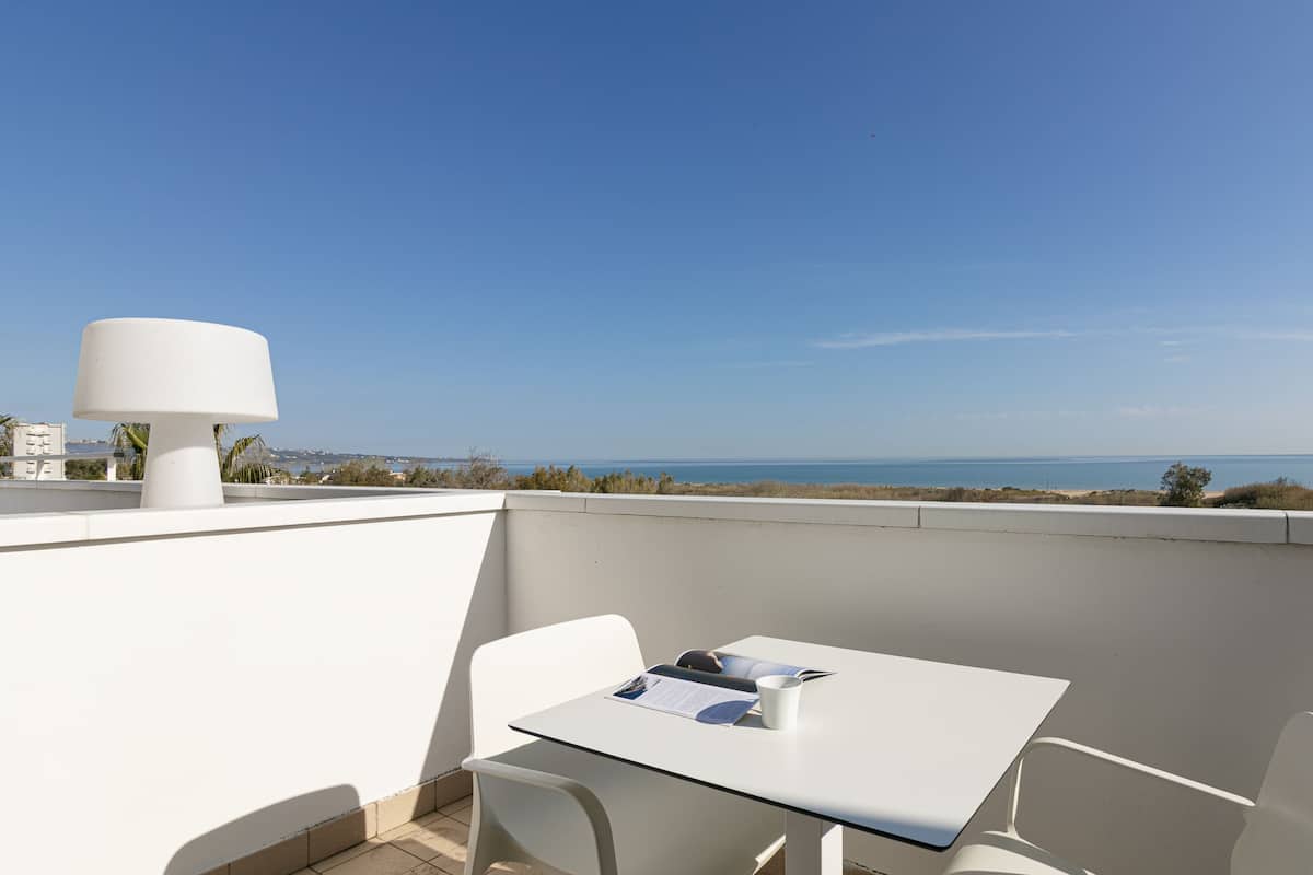 A balcony with a table and chairs, a lamp, and a view of the sea.