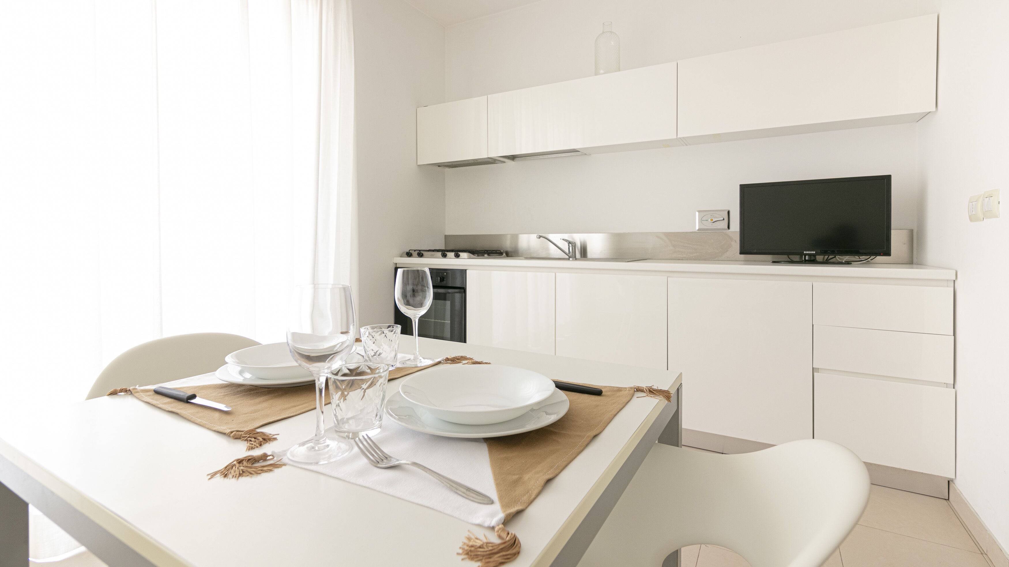 Une cuisine moderne avec des meubles blancs, un four encastré et un téléviseur noir.
