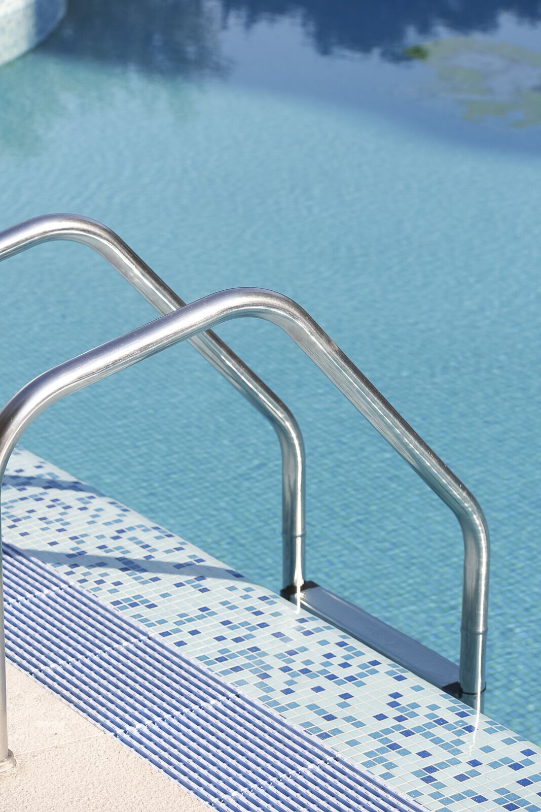 Une échelle métallique pour piscine, dont les marches sont recouvertes de carreaux.