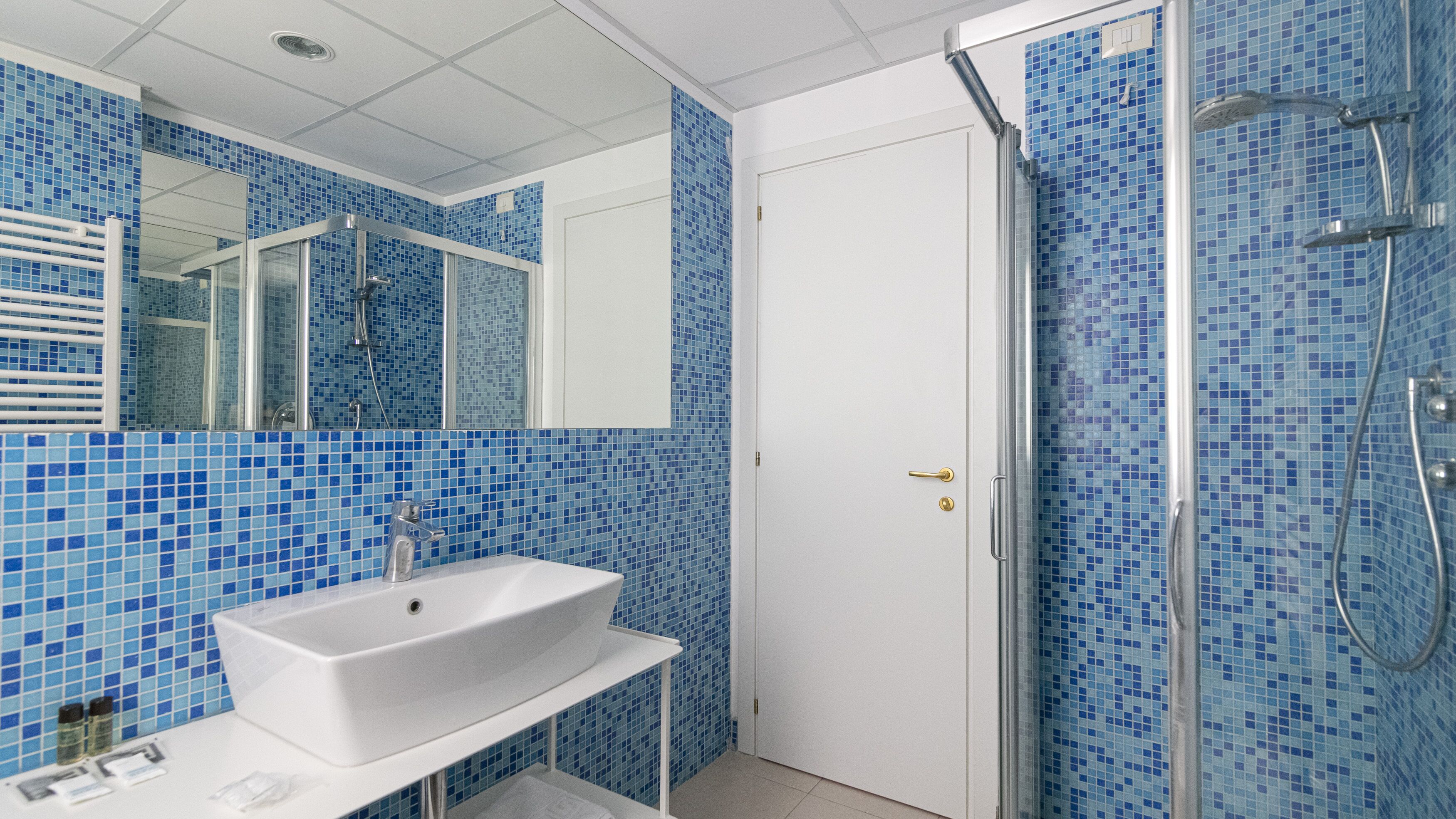 A bathroom with a white sink, a mirror, and a shower with blue mosaic tiles.