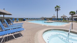A pool area with lounge chairs and umbrellas, a hot tub, and a clear view of the ocean. - Stunning Remodeled Condo on the Beach! Resort Pools, Hot Tubs, Tennis Courts & More! Dog-Friendly! (South Padre Island)