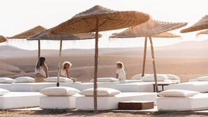 A desert resort with outdoor seating areas under thatched umbrellas, surrounded by white cushioned loungers. - Emeraude Camp Agafy (Agafay)