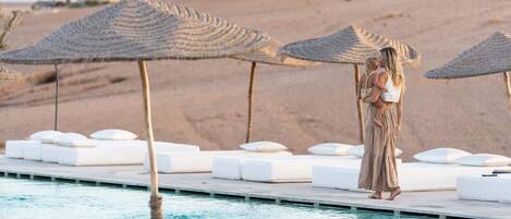 A poolside area with lounge chairs and thatched umbrellas.