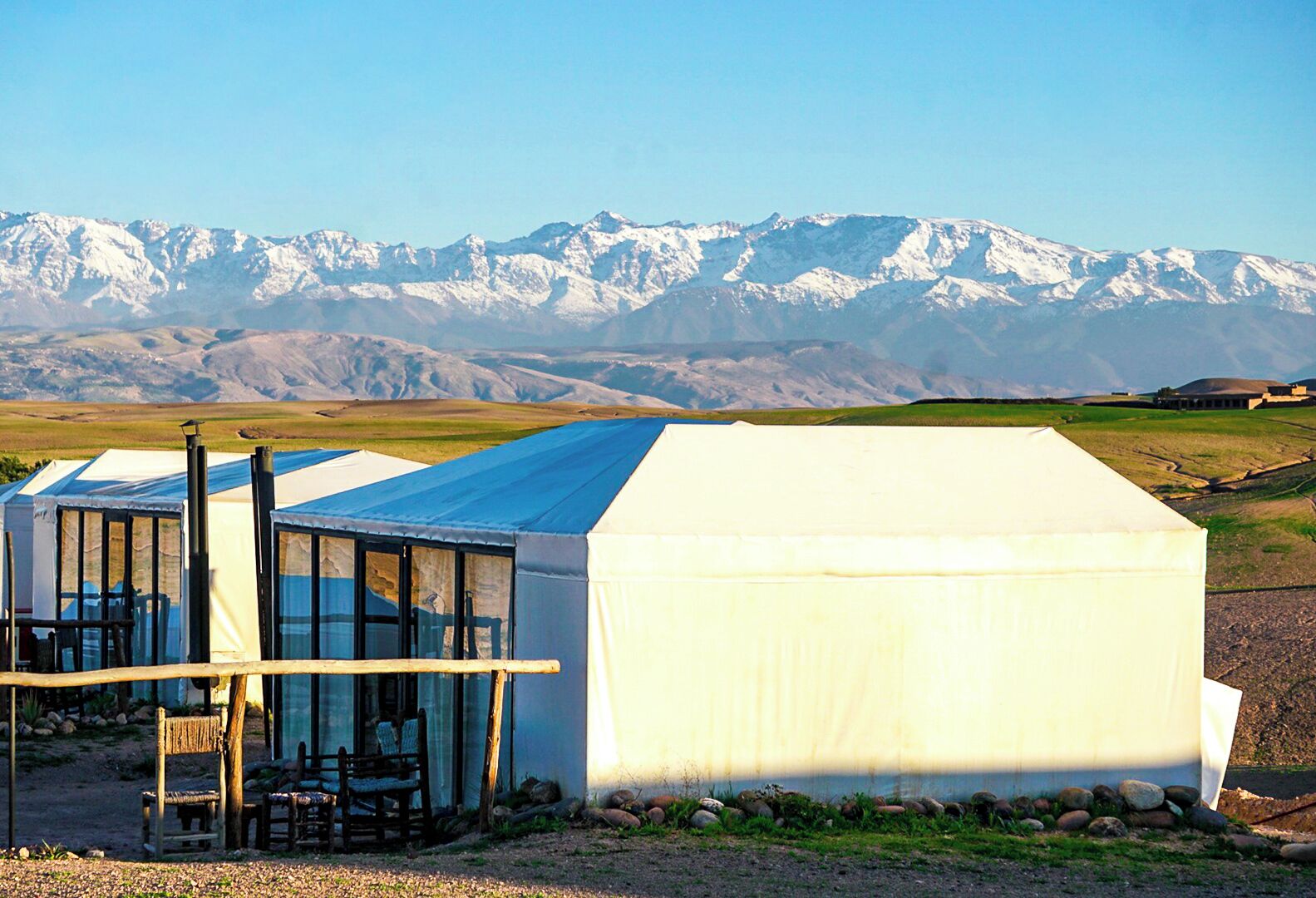 Un bâtiment moderne à toit de verre et à l’extérieur blanc, qui se détache sur le paysage avec, en arrière-plan, des montagnes enneigées.