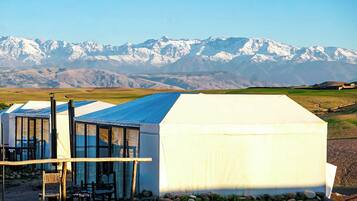 Un edificio moderno con techo de vidrio y fachada blanca, con montañas nevadas al fondo.
