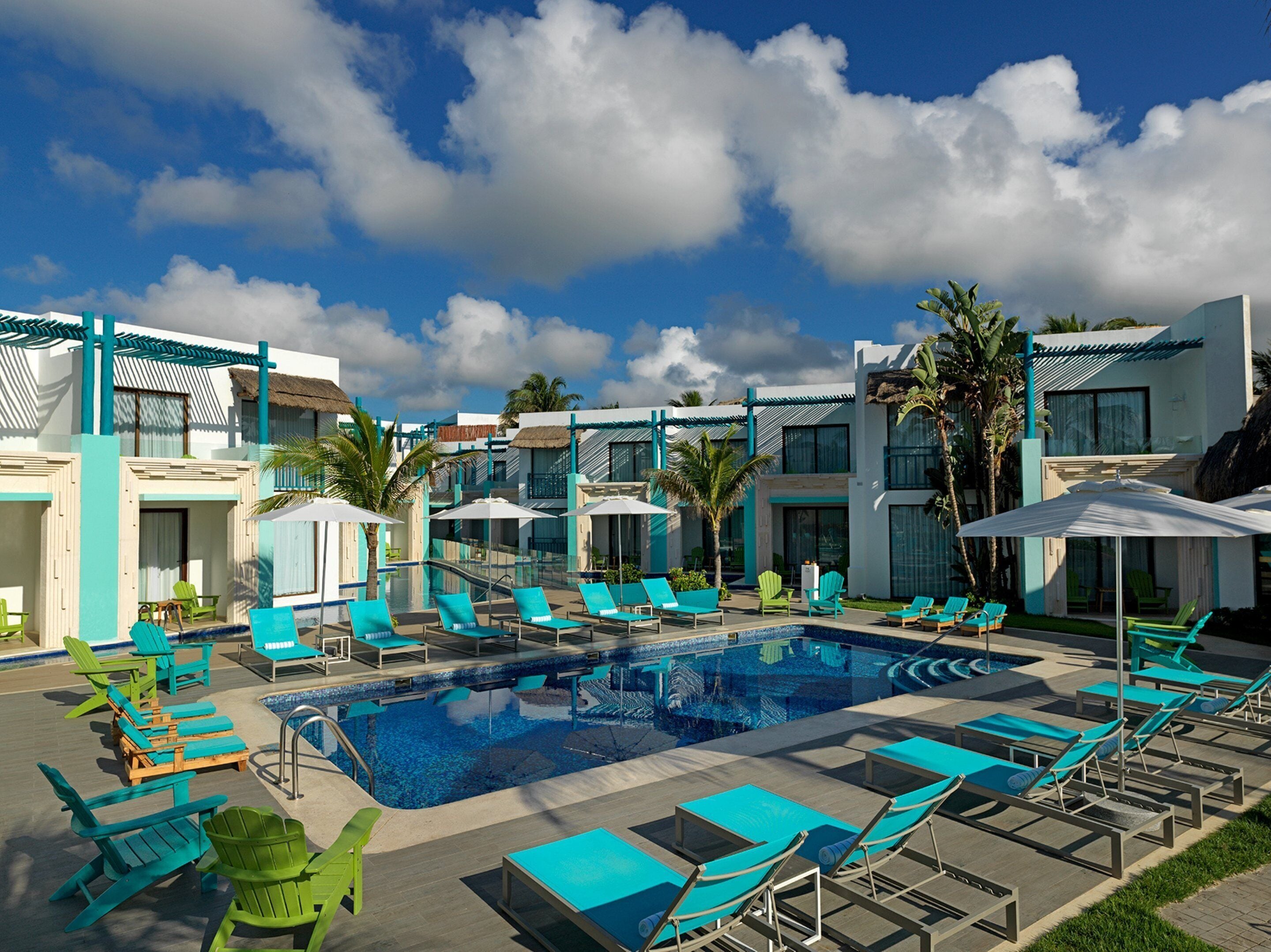 Un espace piscine avec des chaises longues, des parasols et un ciel d’un bleu éclatant.