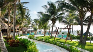 A pool area with palm trees, a lounge chair, and a view of the sea.