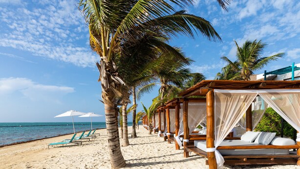 A beach with rows of wooden cabanas and lounge chairs along the shore.