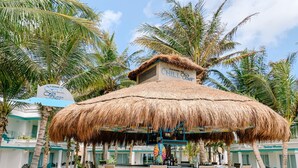 A thatched-roof bar with a circular seating area, surrounded by palm trees and a pool.