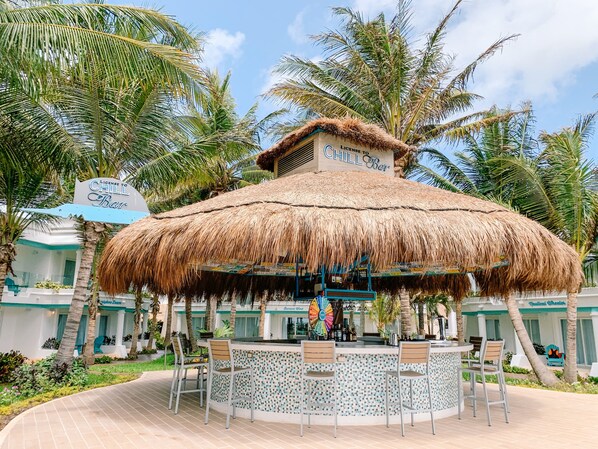 A thatched-roof bar with a circular seating area, surrounded by palm trees and a pool. - Margaritaville Island Reserve Riviera Cancún - A Karisma All-Inclusive Experience for All (Puerto Morelos)